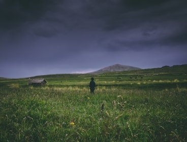 A boy in a field looking out over a stormy sky