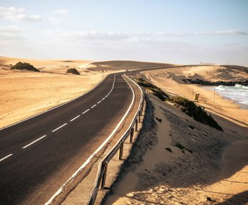 Long black asphalt road with sand dunes and beach to the side