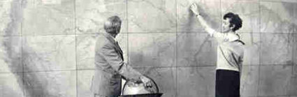 Historic photograph of two people standing in front of large map and with globe.