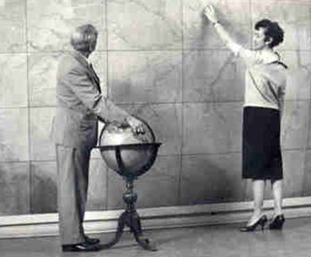 Historic photograph of two people standing in front of large map and with globe.