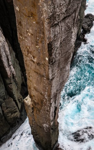 A large coastal stack rock with waves crashing all around the bottom