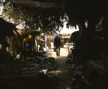 A man walks under a canopy covering a marketplace into the sunlight 