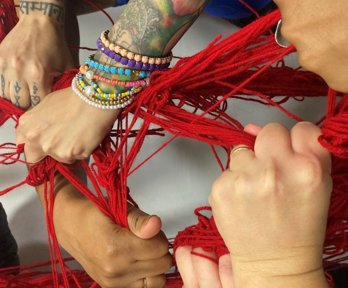 Hands holding onto intertwined strands of knitting wool. 