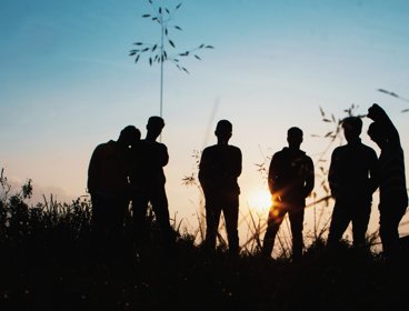 Six people standing in a field with the sun setting behind them