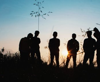Six people standing in a field with the sun setting behind them
