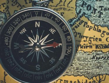 A black compass pointing east, placed on a yellow 'old style' map background
