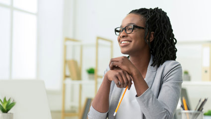 Smiling young professional sitting at a desk in a brightly lit room.