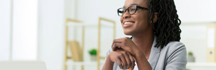 Smiling young professional sitting at a desk in a brightly lit room.