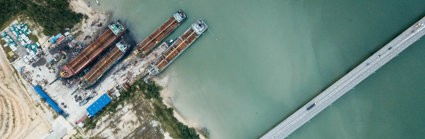 River with a harbour where empty cargo ships have been docked. On the right is a bridge with a road crossing the river.