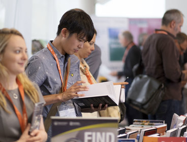 Man wearing a lanyard browsing a book at a publishers stand