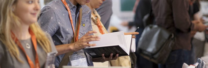 Person wearing a lanyard browsing a book at a publishers stand.