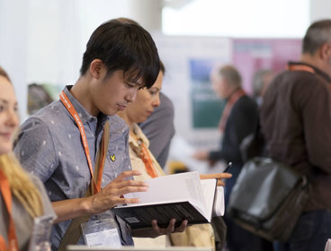 Person wearing a lanyard browsing a book at a publishers stand.