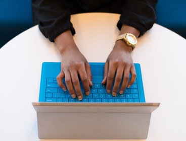 A person typing on a laptop positioned on a round, white table.