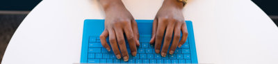 A person typing on a laptop positioned on a round, white table.