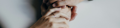 Two people clasp each others pair of hands. Both have rings on, one black and the other's silver.