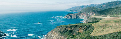 Cliffs covered in vegetation by the sea under a clear sky.