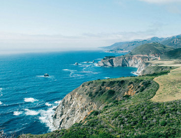 Cliffs covered in vegetation by the sea under a clear sky.