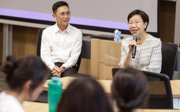 A female professor who is holding a microphone and addressing a group of university staff and students.