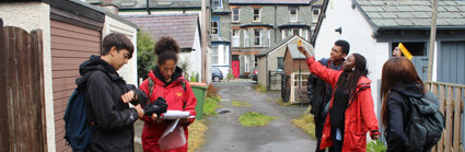 Group of young people taking measurements in a lane behind a row of houses.