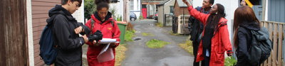 Group of young people taking measurements in a lane behind a row of houses.