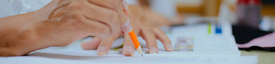 Close-up of a person writing something on paper using a pencil. 