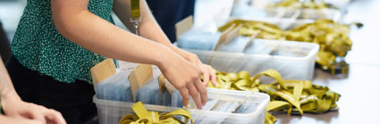 A person sorting green lanyards and badges into plastic boxes.