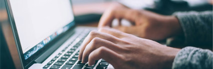 Close up of a person's hands typing on a laptop keyboard.