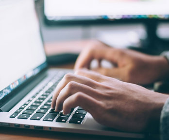 Close up of a person's hands typing on a laptop keyboard.