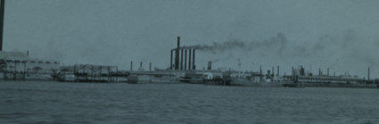 Black and white photograph of a river in the foreground and a factory in the background.