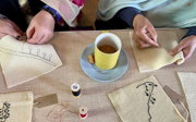 Close up of two people's hand stitching on fabric.