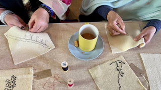 Close up of two people's hand stitching on fabric.