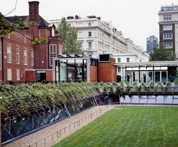 Exterior of the Royal Geographical Society from the garden, showing redbrick building and modern glass Pavilion