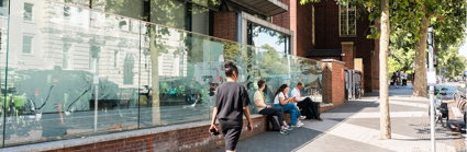 Three people are seated outside the Society's pavilion on a sunny day as one person walks by.