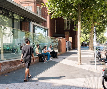 Three people are seated outside the Society's pavilion on a sunny day as one person walks by.