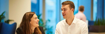 Two people in an office having a conversation and gesturing to one another.