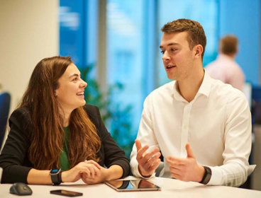 Two people in an office having a conversation and gesturing to one another.