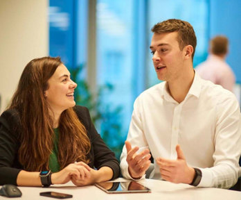 Two people in an office having a conversation and gesturing to one another.