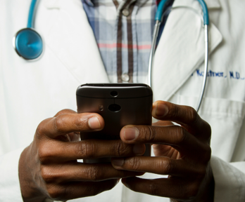 A doctor stands in their lab coat as they type on their phone
