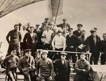 A sepia image of Ernest Shackleton and the crew of Endurance, standing on the ship with sails in the background