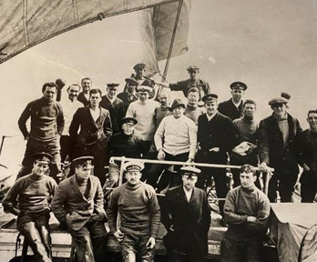 A sepia image of Ernest Shackleton and the crew of Endurance, standing on the ship with sails in the background