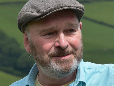 Portrait photograph of Mike Parker standing against backdrop of green fields.