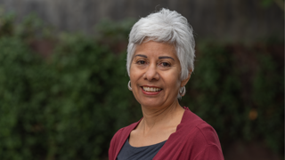 Headshot of Laura Pulido smiling with a blurred out green background.