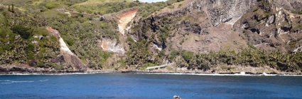 A coastal cliff landscape covered in grassy vegetation with a motor boat moving towards the cliffs.