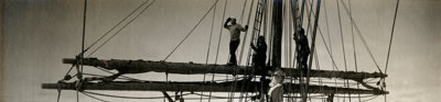 Black and white photograph of the Terra Nova ship, with people standing and sitting on the mast of the ship.