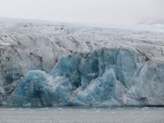 A steep, jagged edge of a glacier adjacent to a lake. 