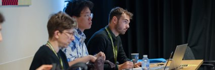 Three conference delegates seated and listening to a conference presentation