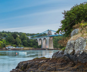 Blue bridge over water with rocks in the foreground