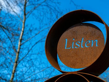 A sign saying ' listen' on a background of blue skye and leafless trees