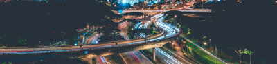 Timelapse photo of a highway with cars in the evening against a background of blue lit highrise buildings.