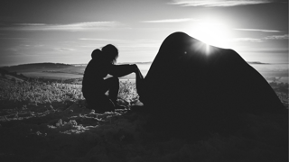 Black and white silhouette of a person camping on a plain.
